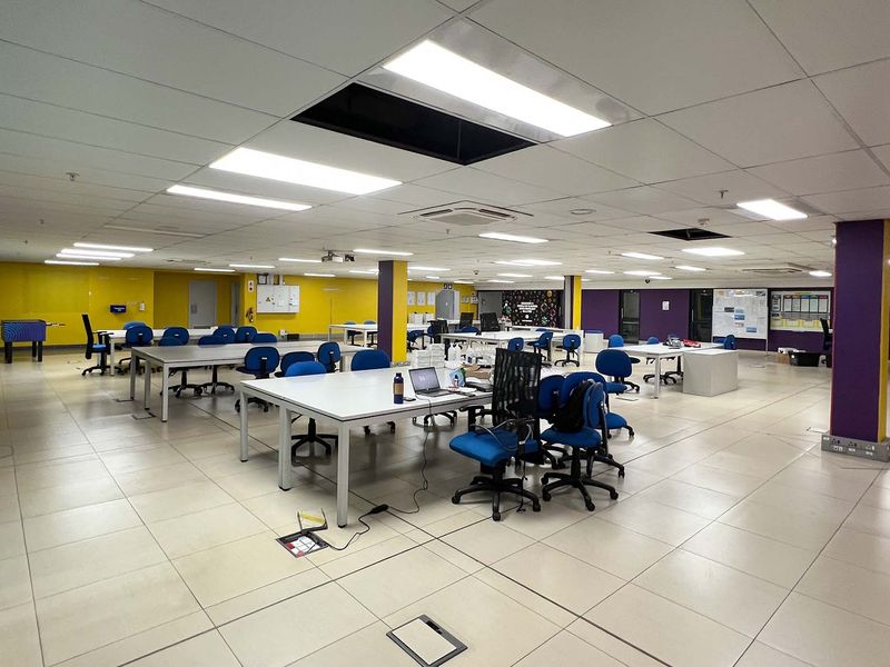 Open-plan industrial office space featuring tiled flooring, suspended ceiling with recessed lighting, and multiple support columns.