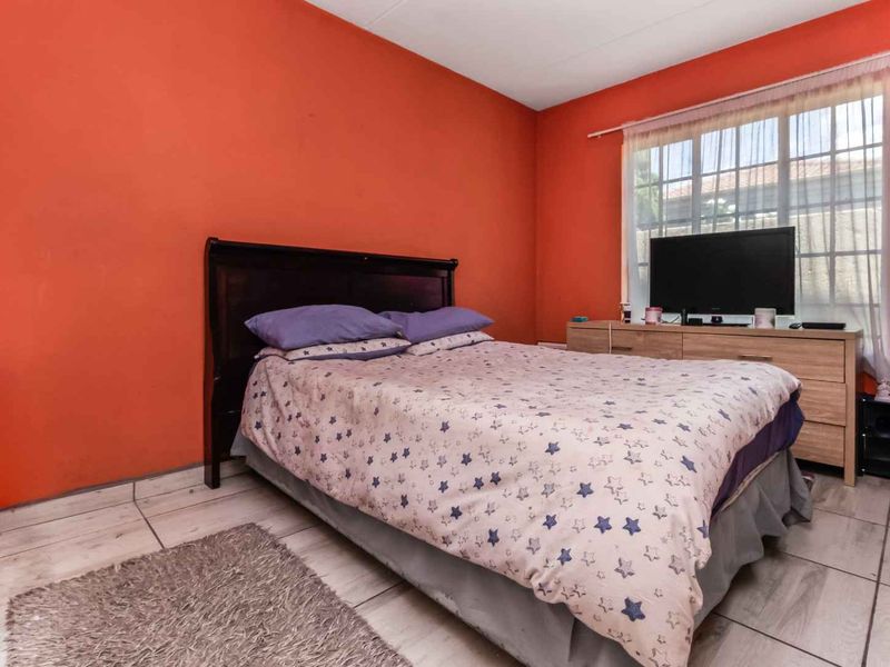 A bedroom featuring tiled flooring and a window with security bars, currently finished with bold orange wall paint.