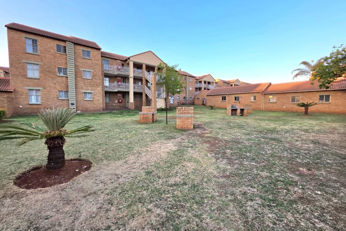 Exterior view of an apartment complex featuring a communal garden area with brick braai facilities and multi-story residential units with balconies.