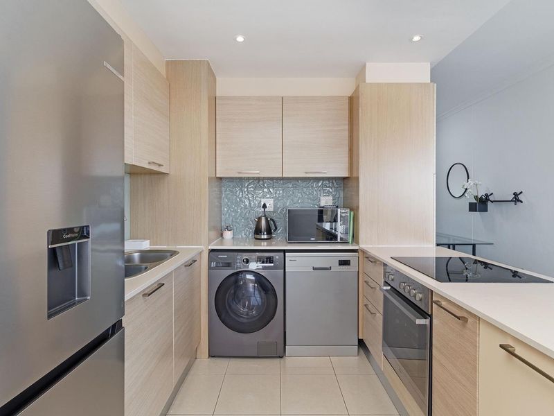 Modern galley-style kitchen featuring light wood cabinetry, stone countertops, integrated appliances, and a stylish textured glass backsplash.