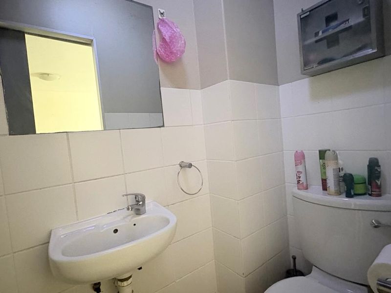 A functional bathroom featuring a wall-mounted basin with chrome mixer tap, toilet, and tiled walls, providing a practical and compact space.