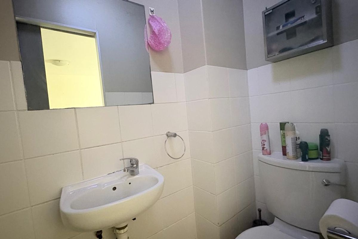 A functional bathroom featuring a wall-mounted basin with chrome mixer tap, toilet, and tiled walls, providing a practical and compact space.