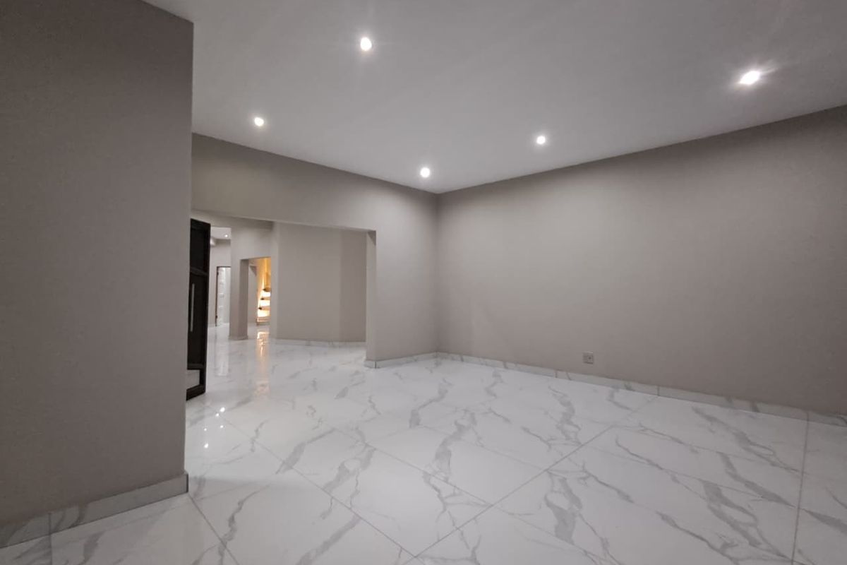 A spacious, empty living area featuring modern white marble-look floor tiles, recessed ceiling lighting, and neutral wall finishes.