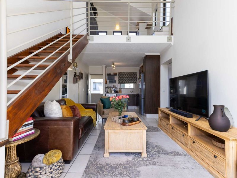 Open plan living area featuring a wooden staircase leading to a mezzanine level, tiled flooring, and an integrated kitchen space.