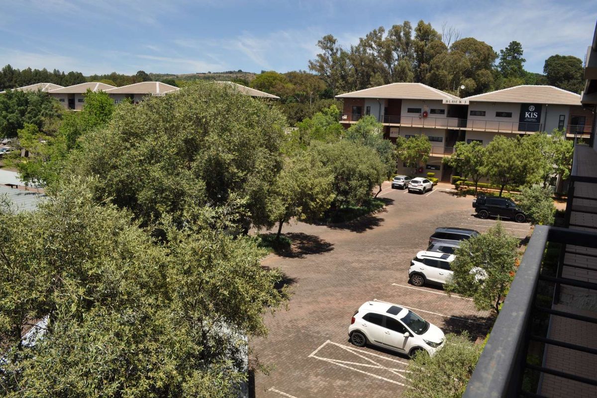Elevated view of an office park complex featuring a paved parking area, mature trees, and multi-story office buildings with tiled roofs.