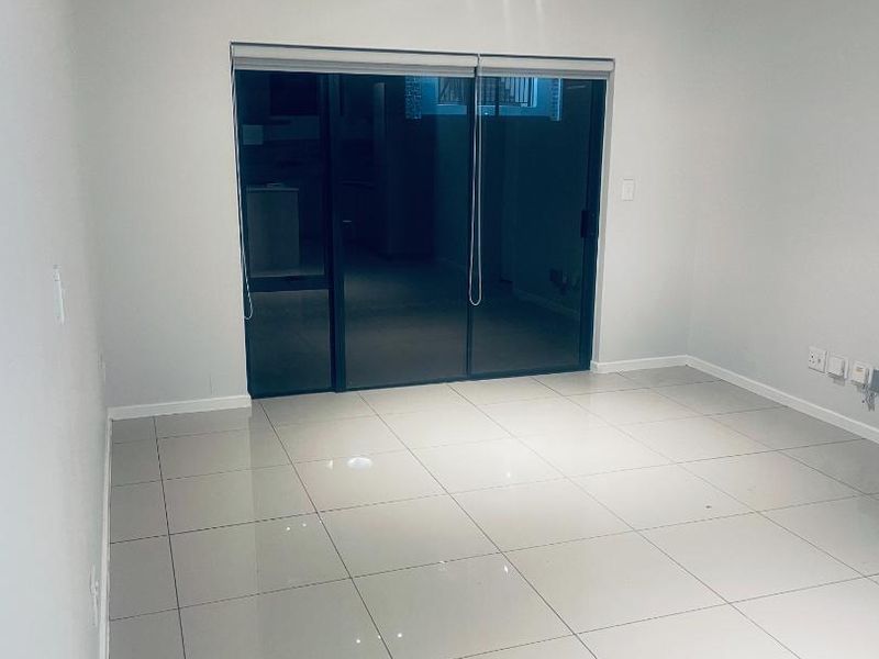 A bright, empty living room featuring large format floor tiles, neutral walls, and a sliding glass door leading to an outdoor area.