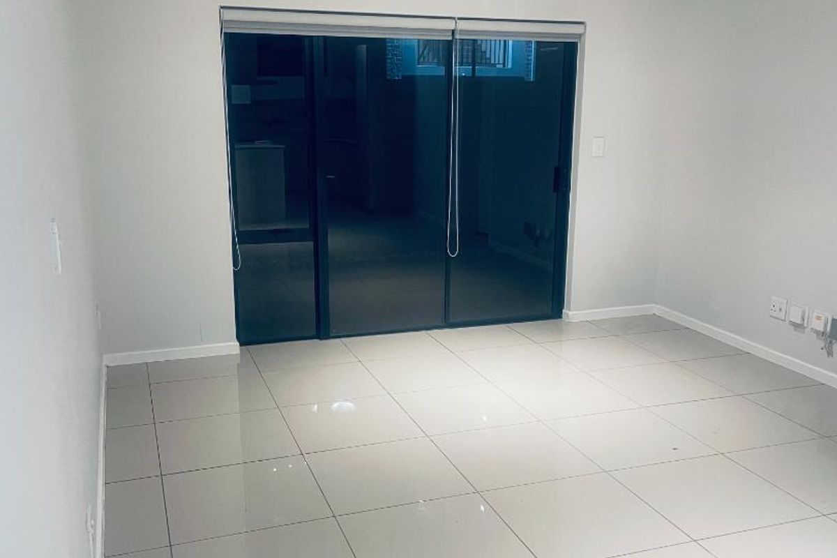 A bright, empty living room featuring large format floor tiles, neutral walls, and a sliding glass door leading to an outdoor area.