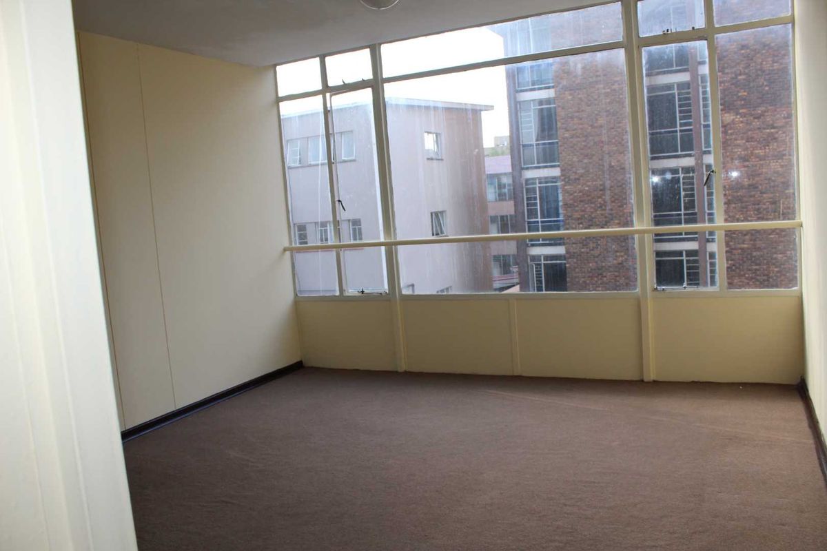 An empty bedroom featuring large windows with urban views and carpeted flooring, offering a blank canvas for renovation.