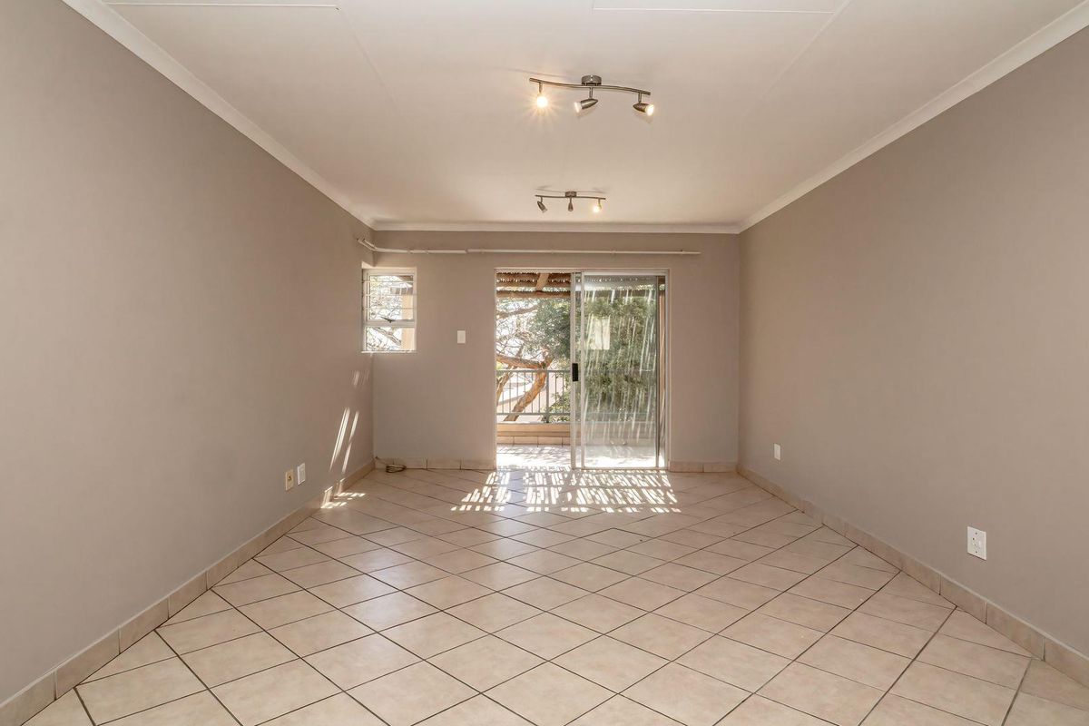 A spacious, empty living room featuring neutral walls, tiled flooring, and a sliding glass door providing access to an outdoor area.