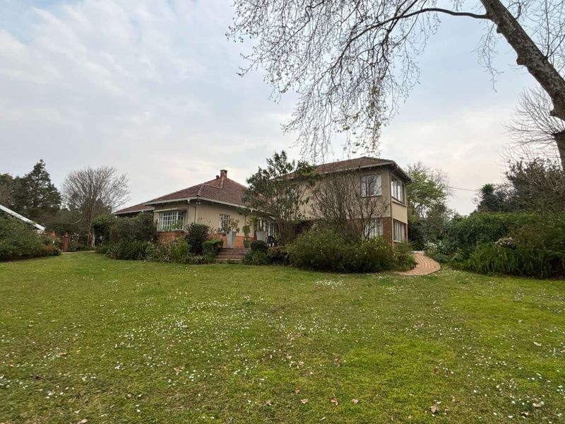 A view of the rear elevation of the house, featuring a large established garden, paved pathways, and traditional brick and tile construction.