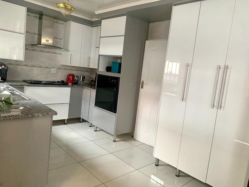 Modern kitchen featuring white high-gloss cabinetry, granite countertops, built-in oven, gas hob, and tiled flooring.