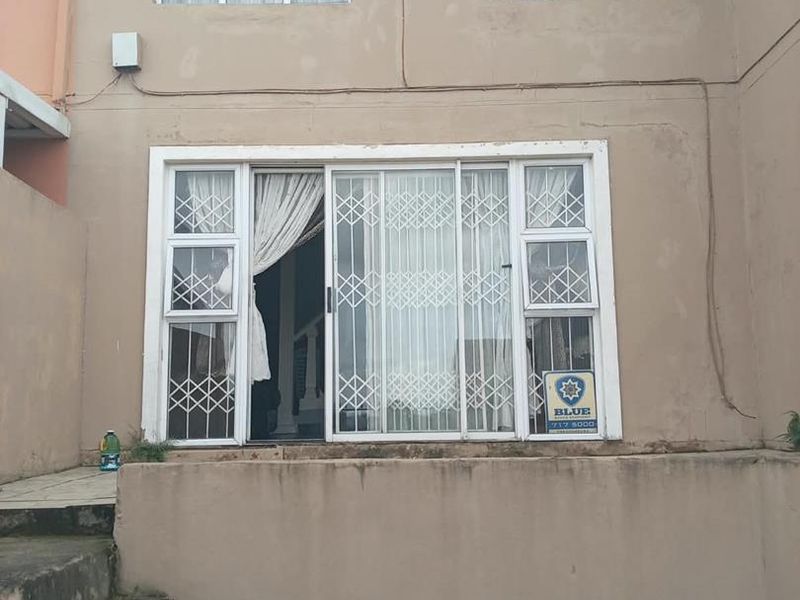 Rear exterior view of the apartment featuring a sliding glass door with security gate, upper-level casement windows, and concrete stairs leading to the entrance.