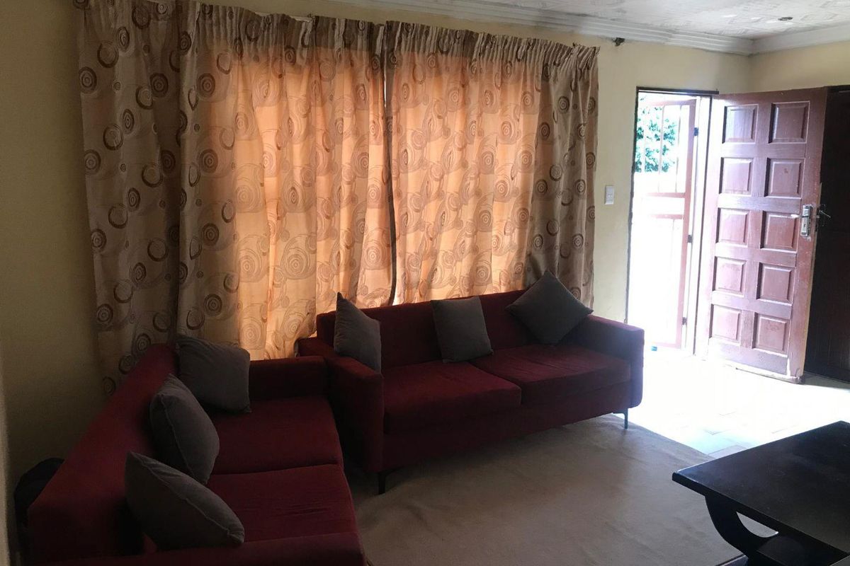 A living room area featuring a tiled floor, a wooden entrance door, and large windows covered by curtains.