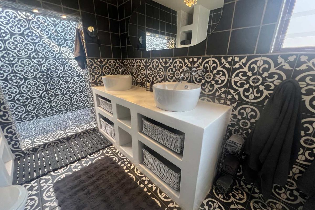 Modern bathroom featuring a double vanity with vessel sinks, walk-in shower, and striking patterned wall and floor tiles.