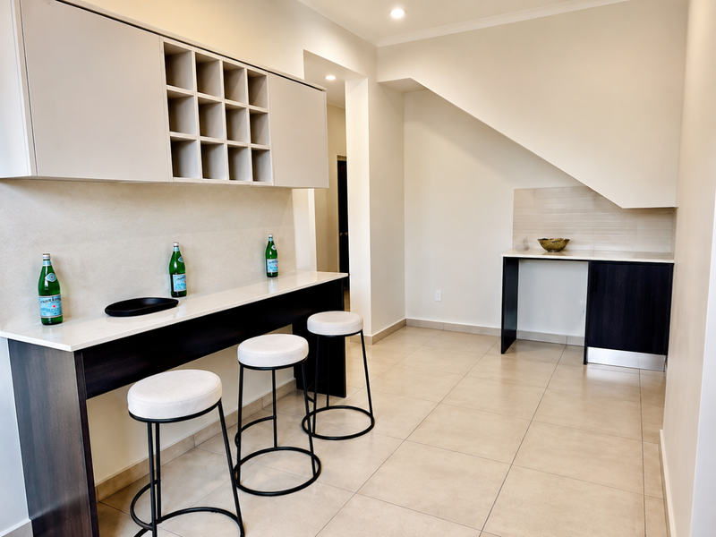 A modern kitchen area featuring built-in cabinetry, a sleek stone breakfast bar, and neutral tiled flooring under a sloped ceiling.