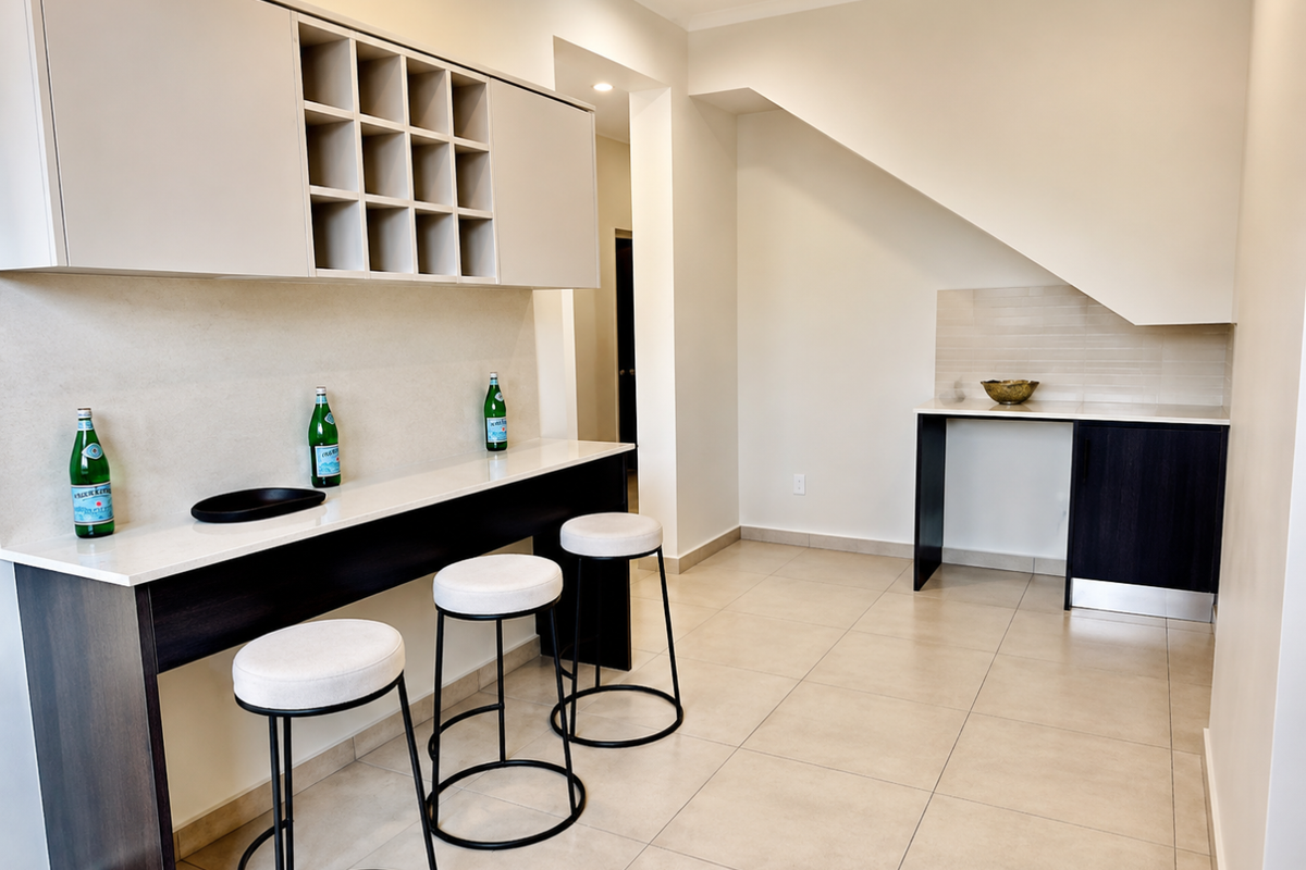 A modern kitchen area featuring built-in cabinetry, a sleek stone breakfast bar, and neutral tiled flooring under a sloped ceiling.