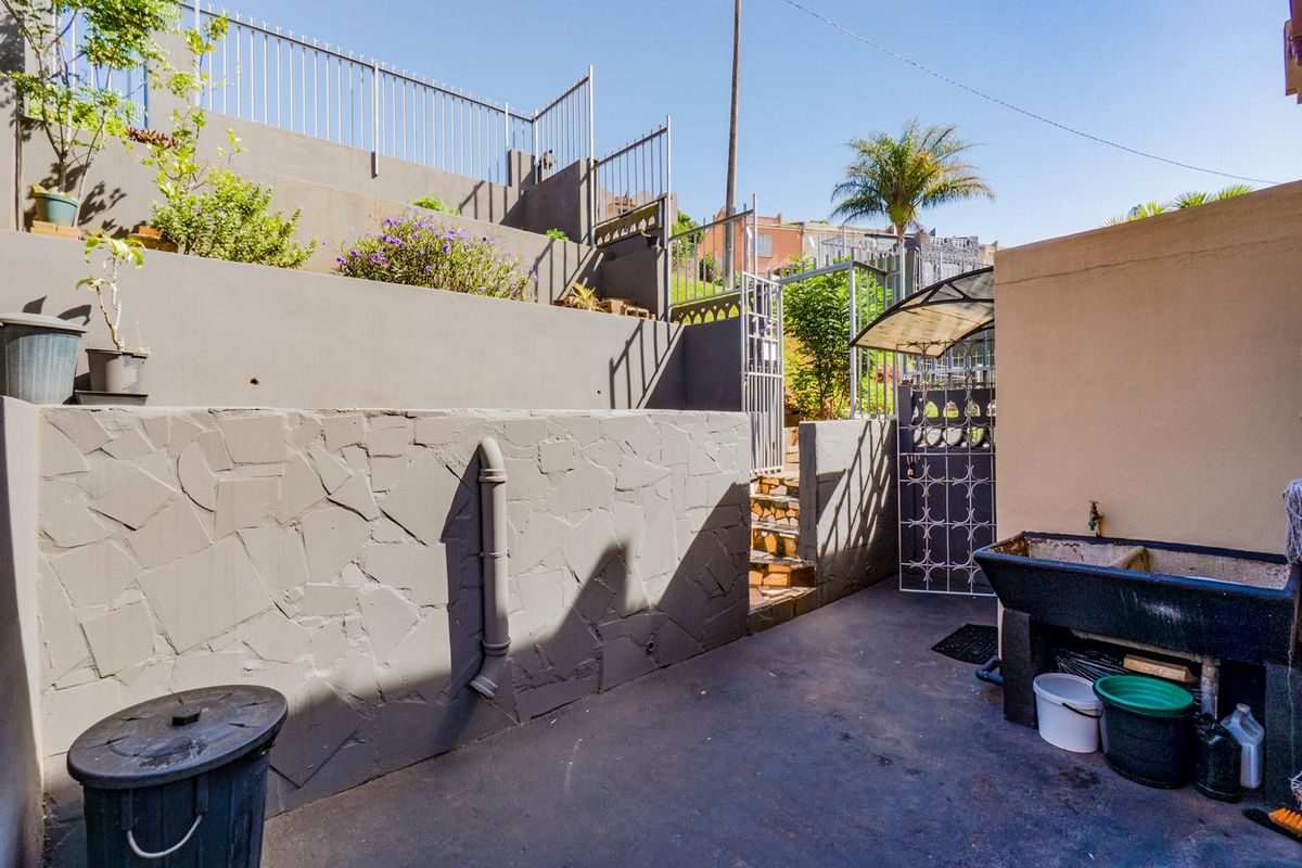 A paved outdoor utility area featuring tiered retaining walls, metal security fencing, and a built-in wash trough.