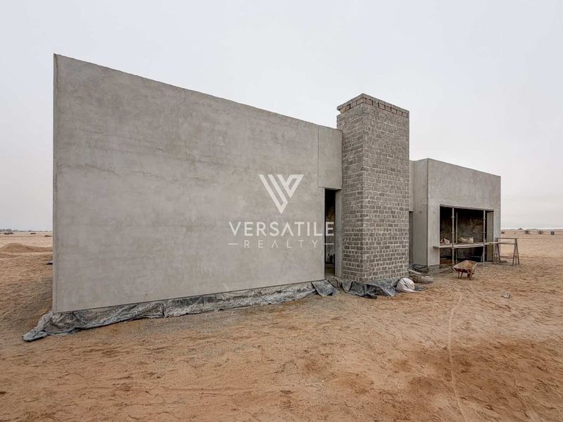 A view of a property under construction featuring cement rendered walls and an exposed brick chimney stack in a desert landscape setting.