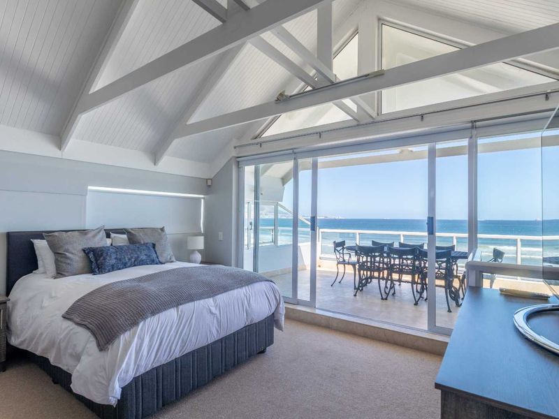 Spacious bedroom featuring a vaulted ceiling with exposed beams, carpeted flooring, and large sliding glass doors opening onto a balcony with ocean views.