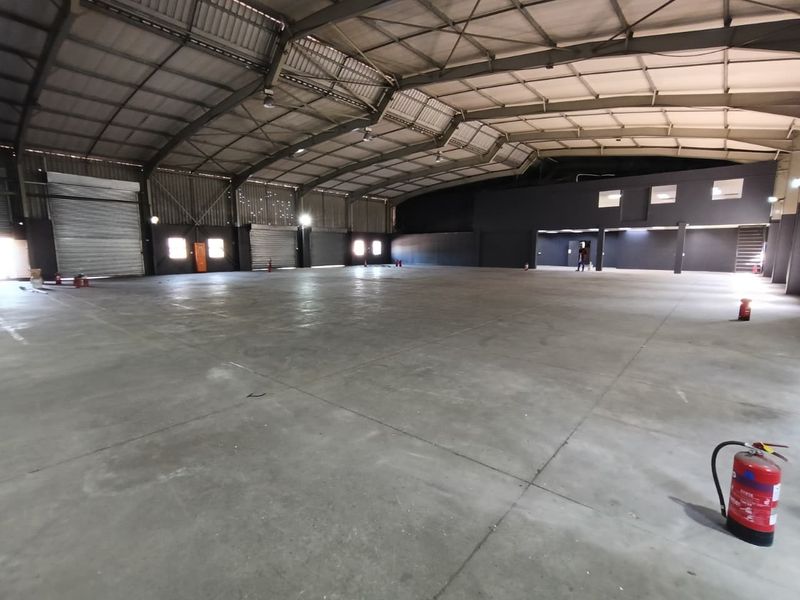 Spacious industrial warehouse featuring high ceilings, concrete flooring, roller shutter access, and a mezzanine level, suitable for various commercial or storage operations.