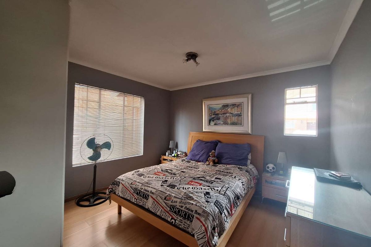 A well-lit bedroom featuring laminate flooring, neutral grey walls, and venetian blinds, providing a comfortable and functional living space.