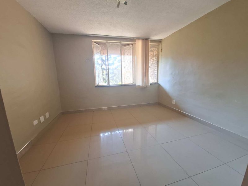 An empty bedroom featuring neutral tiled flooring and large windows with security bars, offering a blank canvas for personalization.