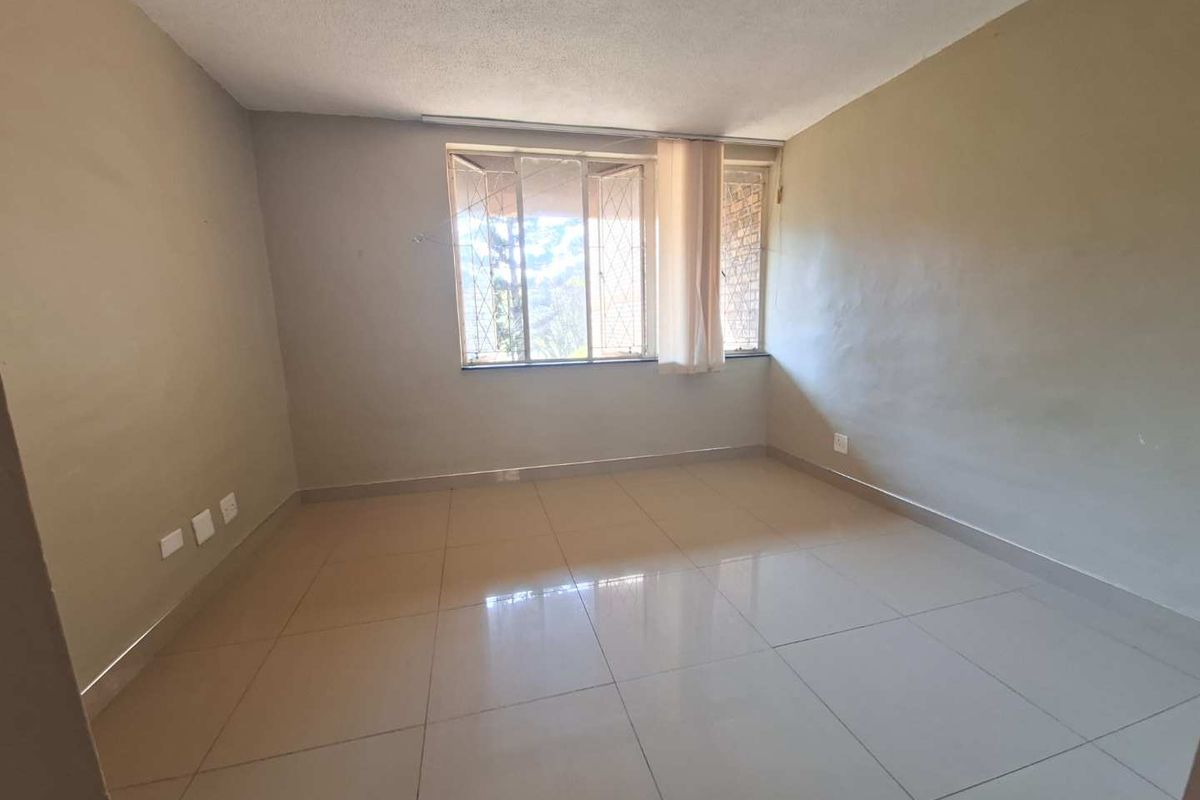 An empty bedroom featuring neutral tiled flooring and large windows with security bars, offering a blank canvas for personalization.