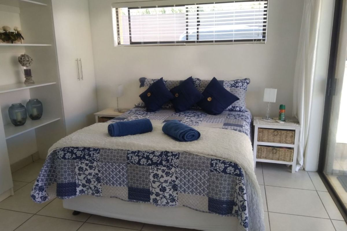 A bright bedroom featuring built-in shelving, integrated wardrobe storage, tiled flooring, and a sliding glass door providing access to the exterior.
