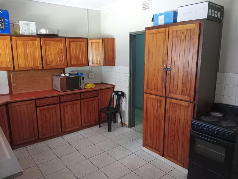 A dated kitchen featuring wooden cabinetry, tiled flooring, a tiled backsplash, and a freestanding stove, offering potential for modernization and renovation.