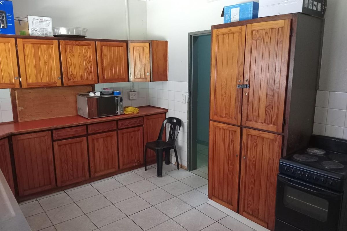 A dated kitchen featuring wooden cabinetry, tiled flooring, a tiled backsplash, and a freestanding stove, offering potential for modernization and renovation.