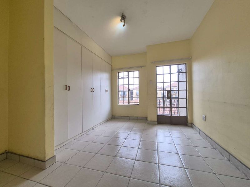 An empty bedroom featuring tiled flooring, built-in cupboards, and a glass door leading to a balcony, offering a blank canvas for personalization.