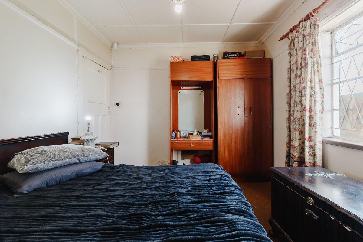 A bedroom featuring a built-in wooden wardrobe, tiled ceiling, and security bars on the window. The room requires cosmetic updates to the walls and ceiling.