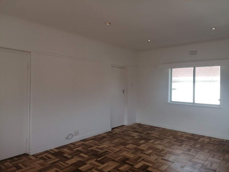 A bright, empty bedroom featuring well-maintained parquet flooring, recessed ceiling lighting, and neutral white walls.