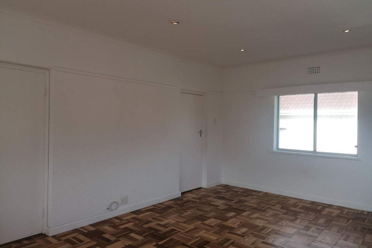 A bright, empty bedroom featuring well-maintained parquet flooring, recessed ceiling lighting, and neutral white walls.