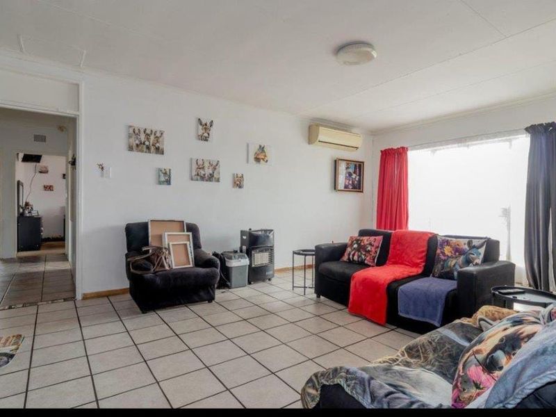 A functional living room featuring neutral tiled flooring, a wall-mounted air conditioning unit, and natural light from a large window.