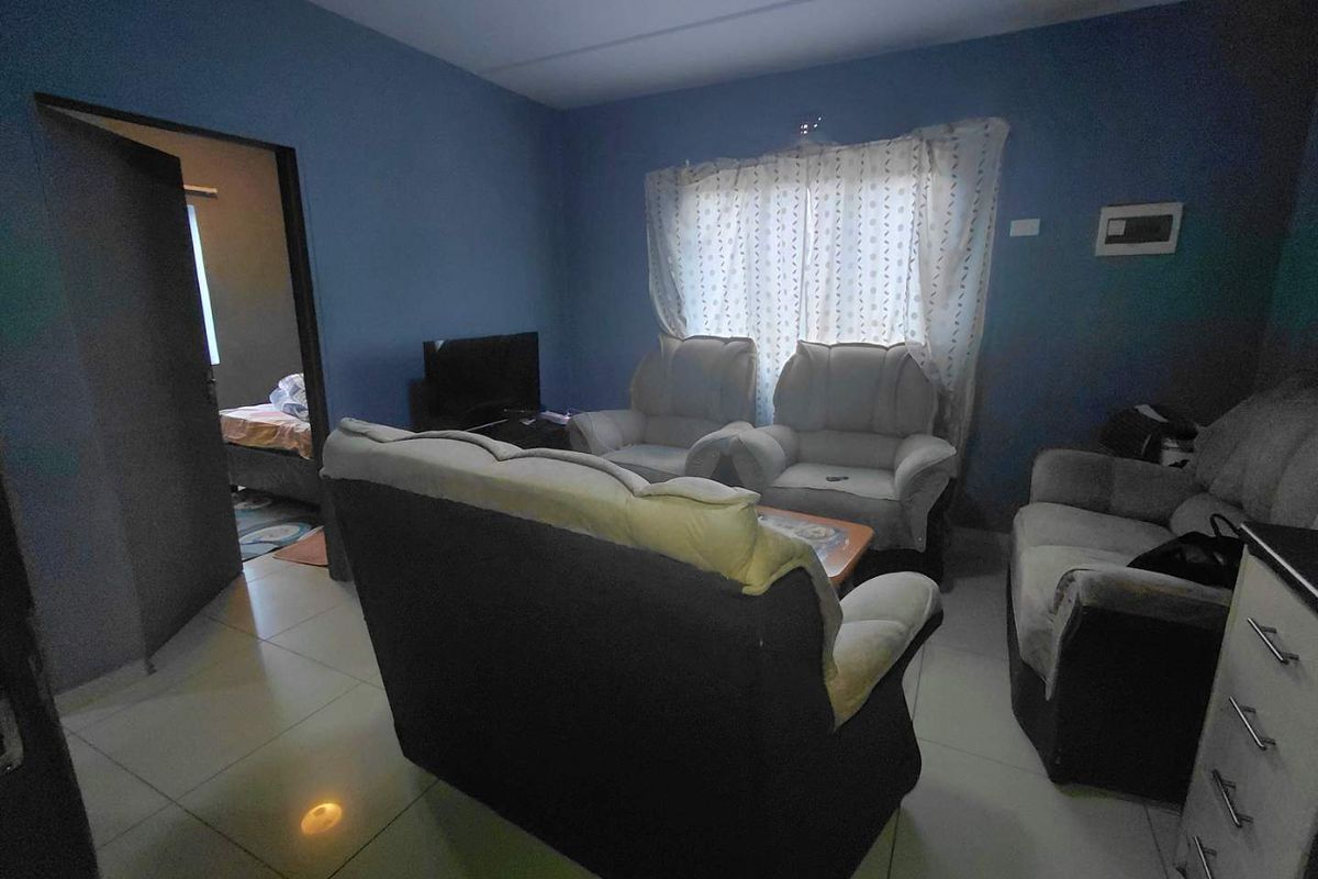 A living room featuring tiled flooring and blue painted walls, with an adjacent bedroom visible through the doorway.