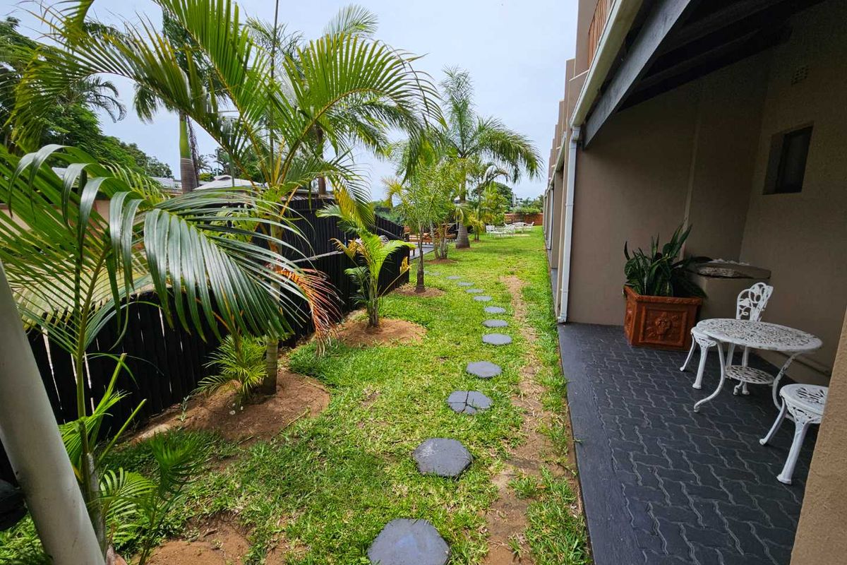 A view of the rear garden featuring a paved patio area, stepping stones, and established palm trees along the building exterior.