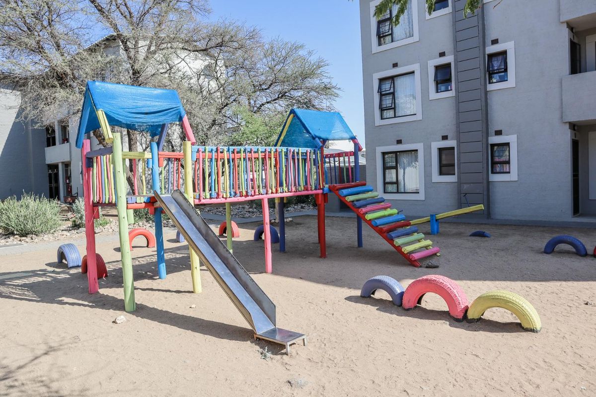 Communal outdoor playground area located at the rear of the apartment complex, featuring fixed play structures and sandy ground surface.