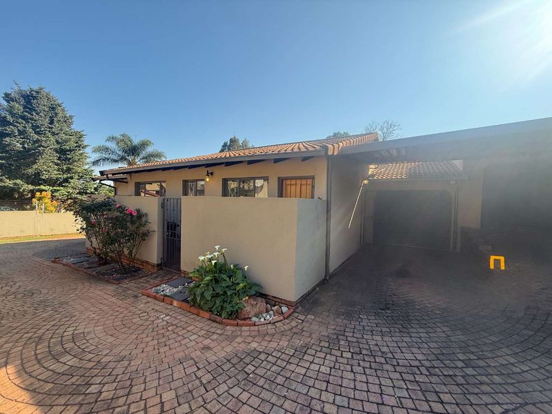 Front exterior view of the townhouse featuring a paved driveway, covered carport, garage, and a private walled entrance area.