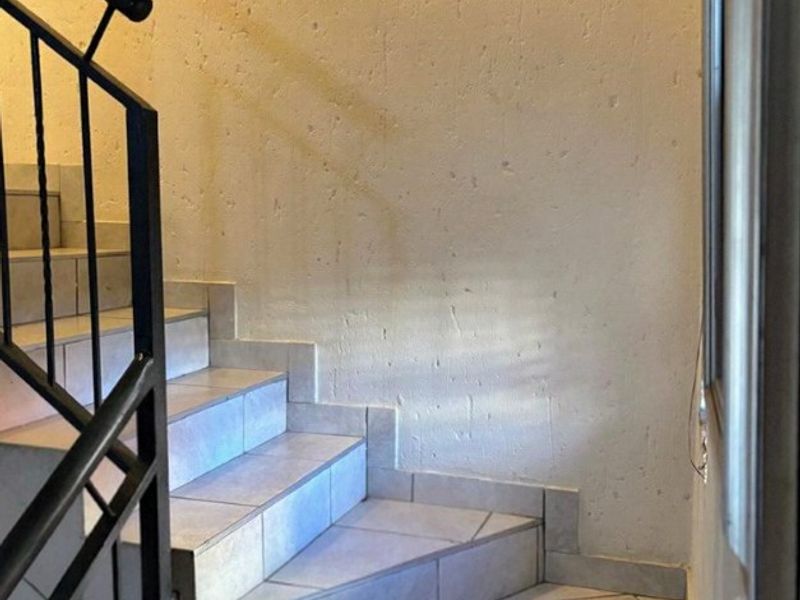 A functional interior staircase featuring tiled steps and a black metal balustrade, providing access between levels within the apartment.