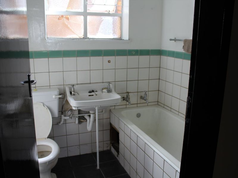 A dated bathroom featuring a built-in bathtub, wall-mounted basin, and toilet, requiring renovation to update the finishes and address visible maintenance issues.