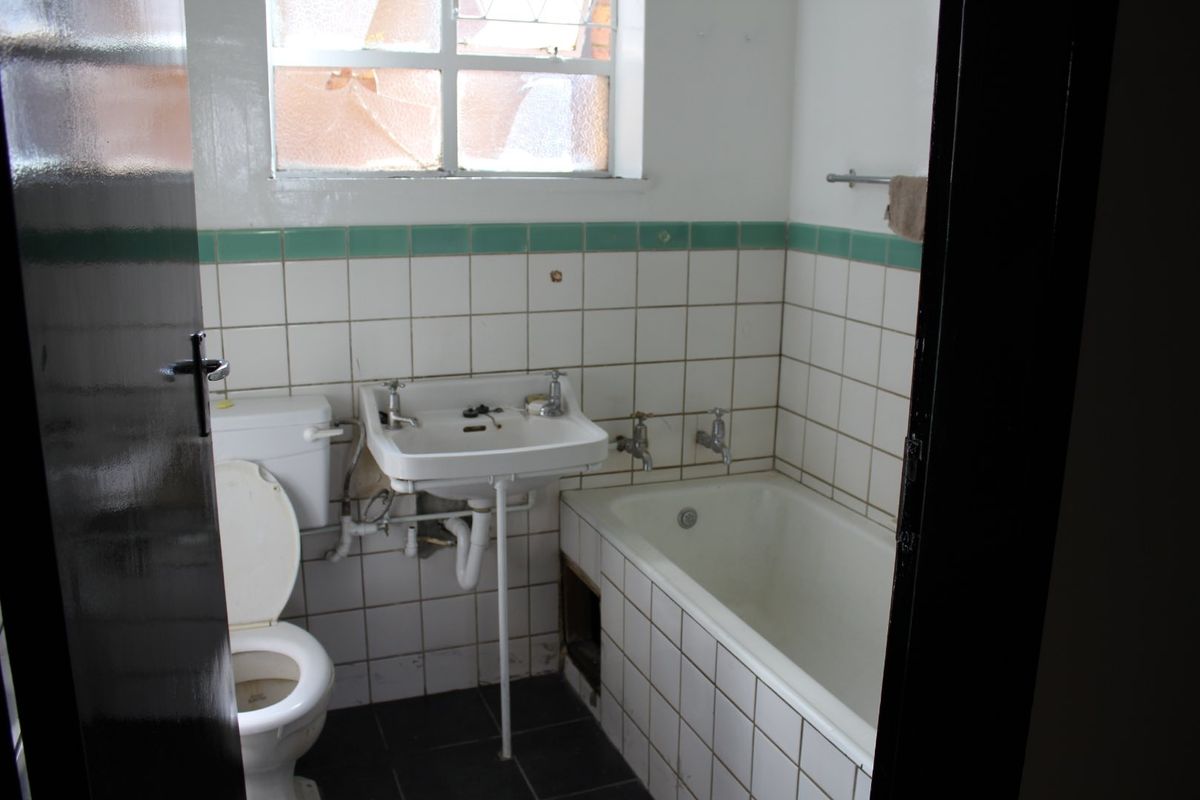 A dated bathroom featuring a built-in bathtub, wall-mounted basin, and toilet, requiring renovation to update the finishes and address visible maintenance issues.