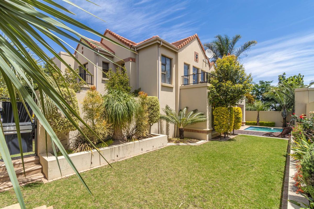 Rear view of the property featuring a landscaped garden, raised planters, a swimming pool, wooden decking, and a balcony overlooking the outdoor area.