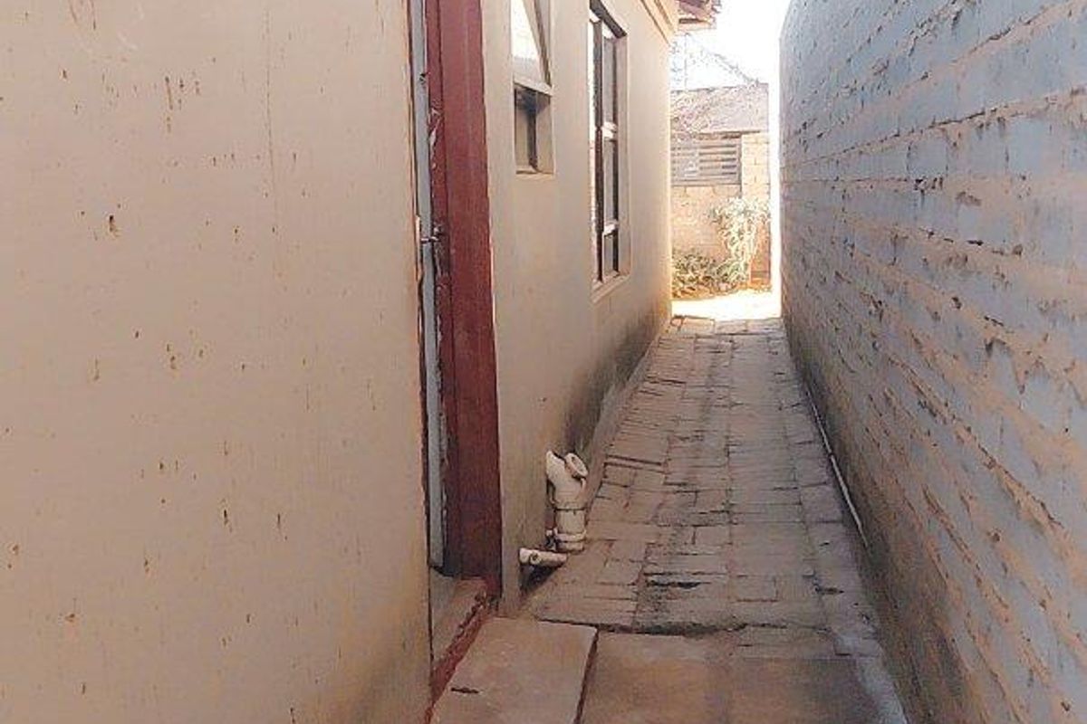 A narrow side passage featuring paved flooring, a brick boundary wall, and access to the side of the house.
