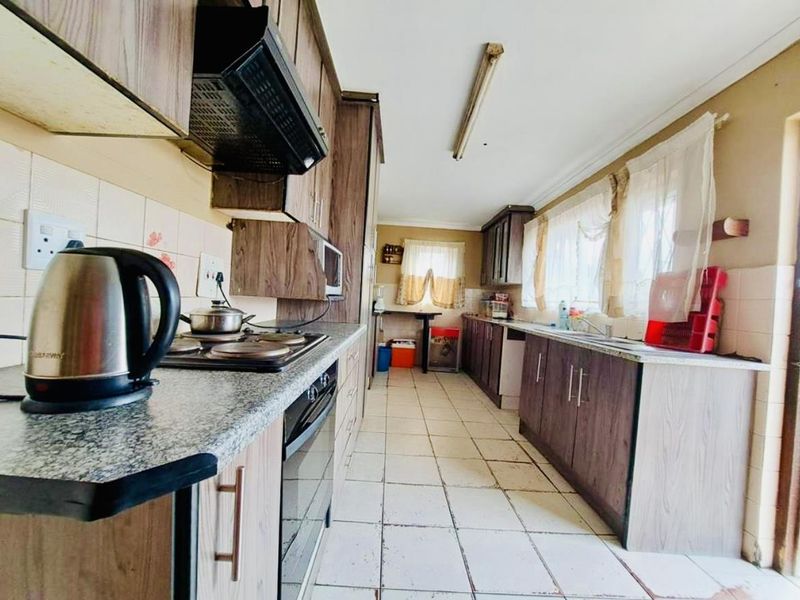 A functional galley-style kitchen featuring laminate cabinetry, granite countertops, built-in oven, electric hob, and tiled flooring throughout.