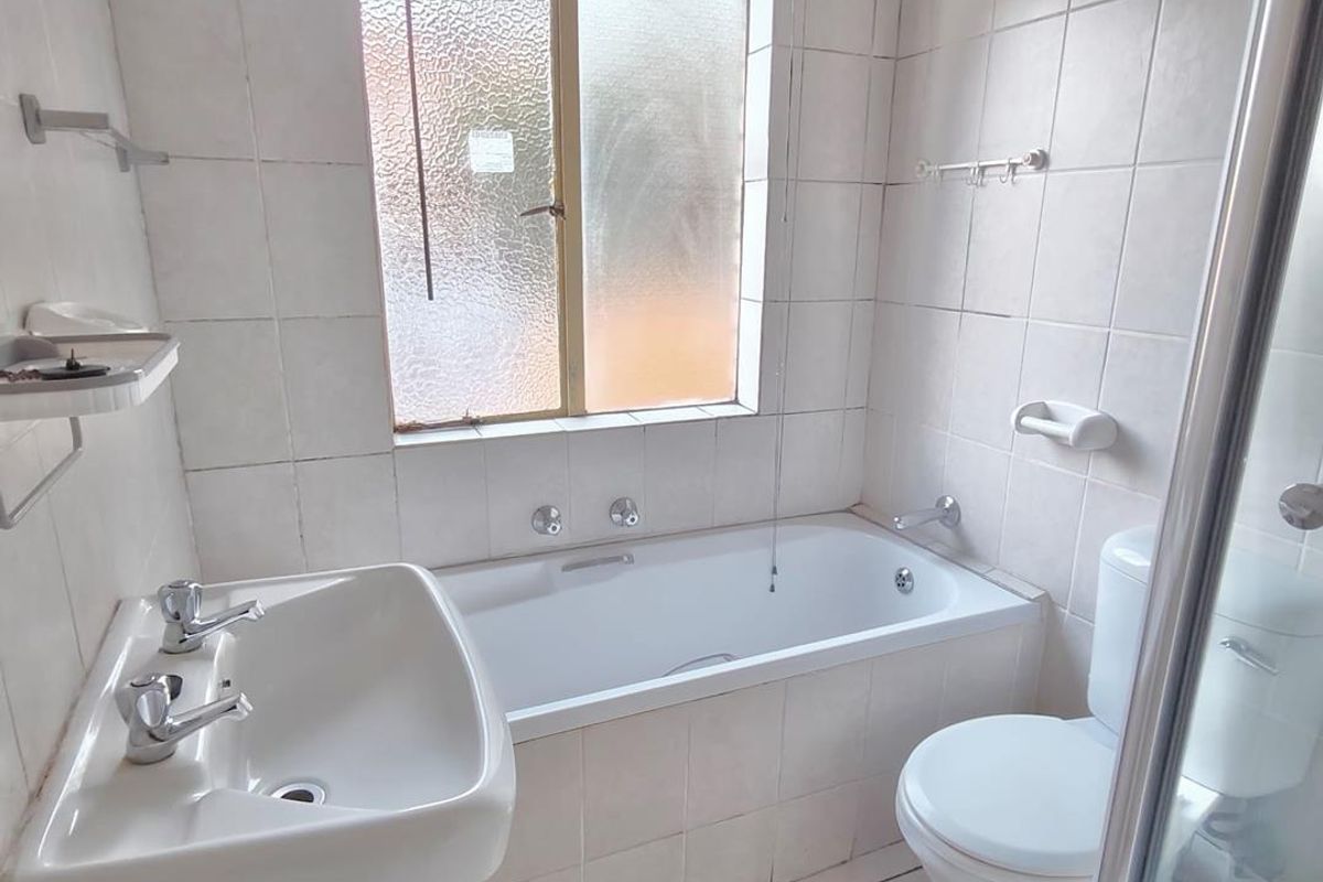 A functional bathroom featuring a pedestal basin, built-in bathtub, toilet, and a separate shower enclosure with tiled finishes throughout.