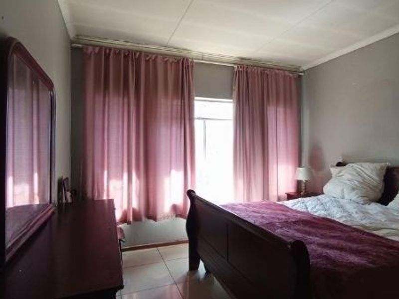 A standard bedroom featuring tiled flooring and natural light through window curtain treatments.