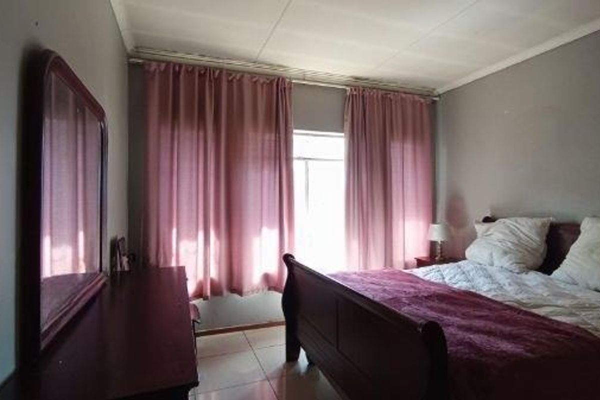 A standard bedroom featuring tiled flooring and natural light through window curtain treatments.