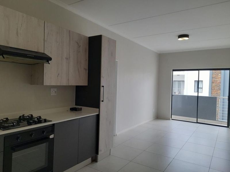 Modern open-plan kitchen and living area featuring contemporary cabinetry, built-in appliances, tiled flooring, and direct access to a private balcony.