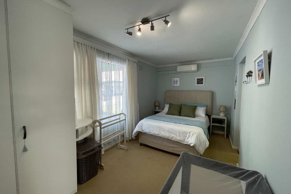 A functional bedroom featuring built-in wardrobe storage, carpeted flooring, and a wall-mounted split-system air conditioning unit.